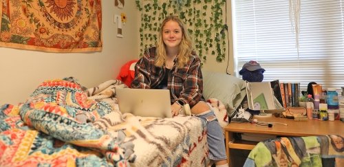 Student using laptop while sitting on bed in residence hall at CU-Mansfield