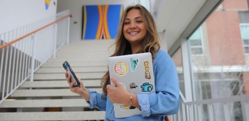 Student  holding a lap top and looking at a cell phone