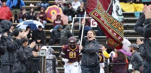 Bloomsburg cheerleader leads football team onto field.