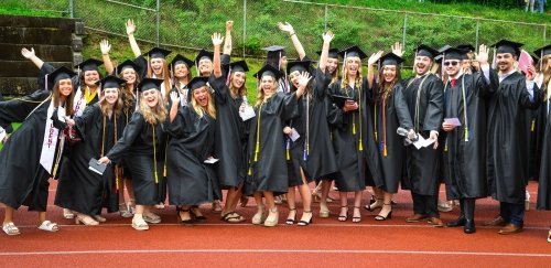 A large group of about 20 Lock Haven Graduates in their caps and gowns celebrate on the university track during commencement