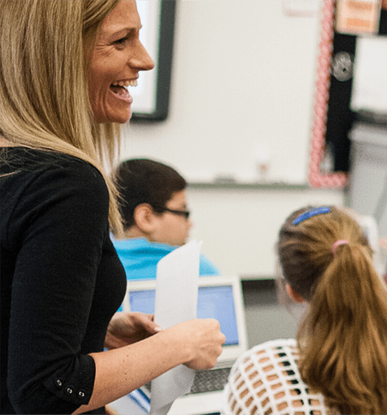 teacher laughing with students in the background on computers