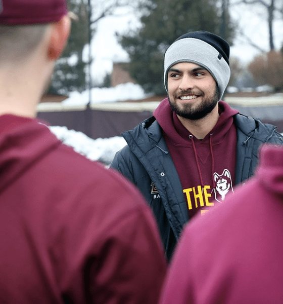 a coach in a Huskey sweatshirt and cap, smiling in front of some players outside in winter