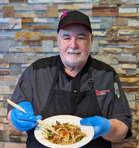 Male food service employee hold food and chopsticks.