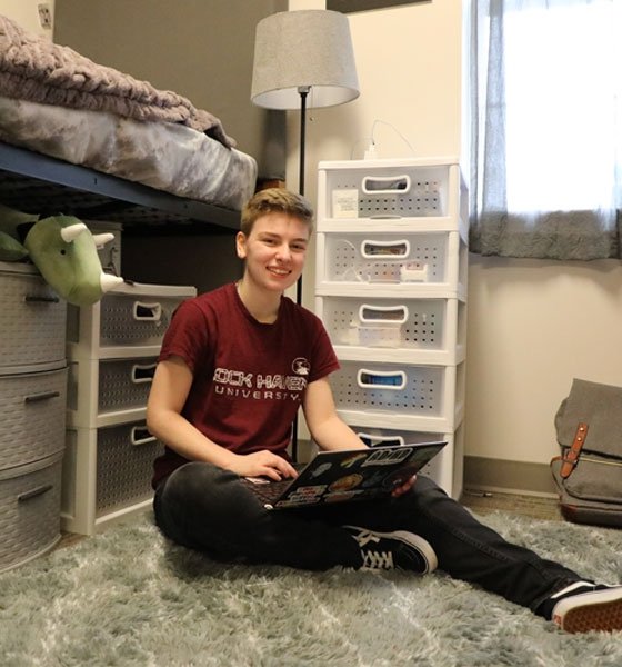 Lock Haven student sitting on floor of their room in Fairview Suites while using a computer.