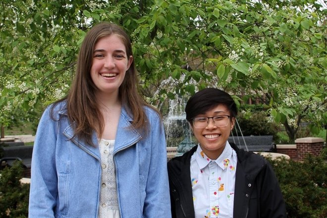 Two people standing side by side in front of some trees. 