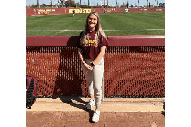 A woman standing by a baseball field. 