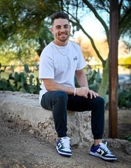 a photo of Jarod Zimmerman smiling outside sitting on a rock