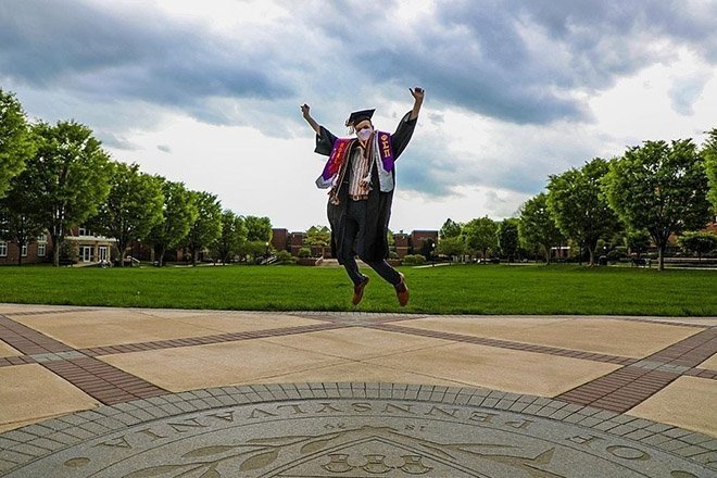 Student jumping in air in graduation robe.