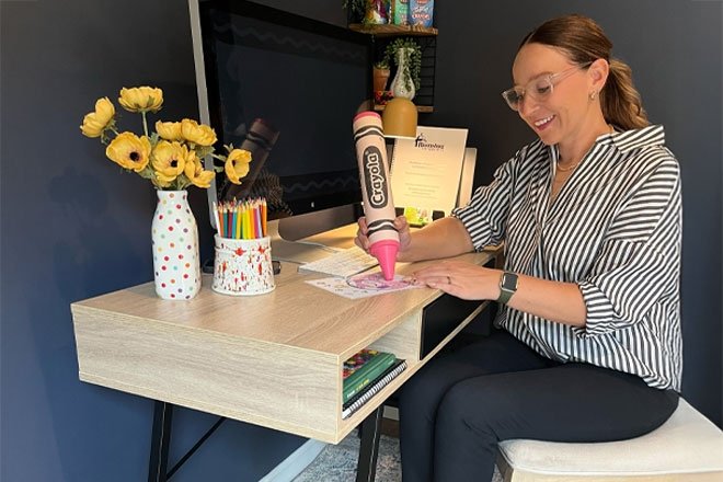 Amanda Williams, Project Manager for Crayola sitting at desk with giant crayon.