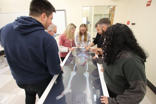 Health Science students surround an Anatomage table for hands-on, simulated instruction