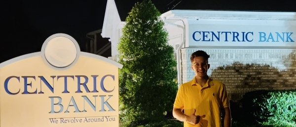 A guy standing by a Centric Bank sign.