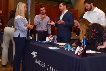 People talking behind a Baker Tilly table. 