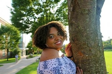 A girl standing by a tree. 