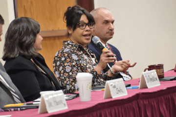 Three people sitting at a table. One is talking in a microphone. 