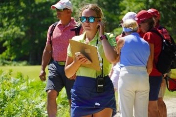 A girl walking with a clipboard with people behind her. 