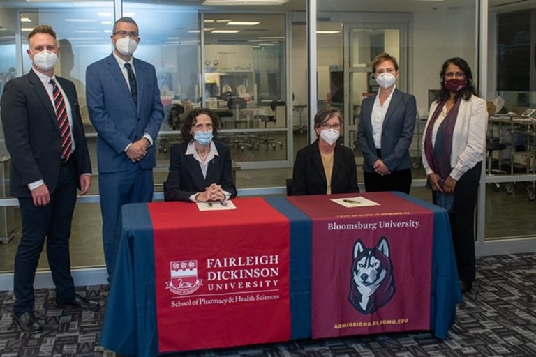 Two people sitting behind a signing table. Four people standing around the table. 