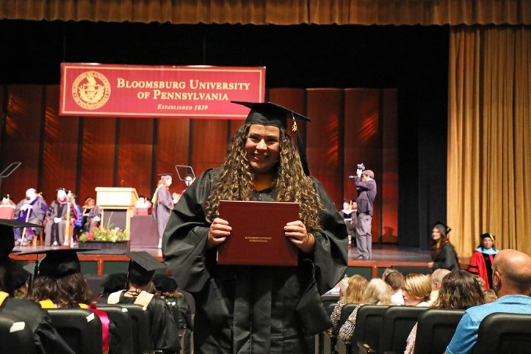 A girl in a graduation cap and gown with a diploma. 