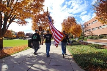 Three people walking on the side walk with an American flag.