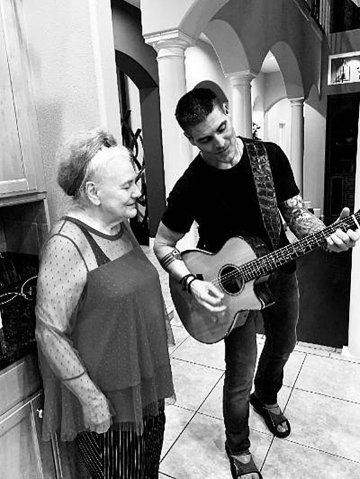 A black and white photo of a guy playing guitar for an older lady.