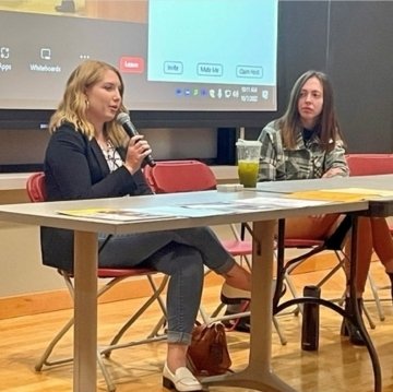 Two women sitting at a table with a microphone. 