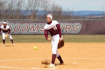 A girl on the softball field throwing a ball. 