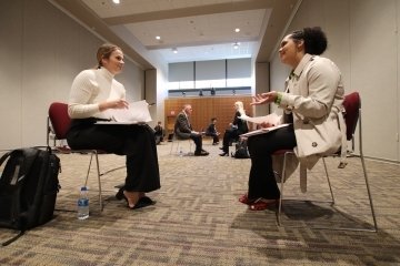 Two girls, sitting in chairs, talking. 