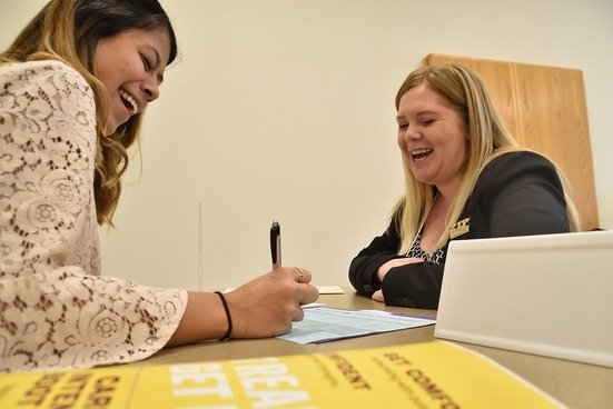 two woman laughing in conversation while filling out forms at a shared desk