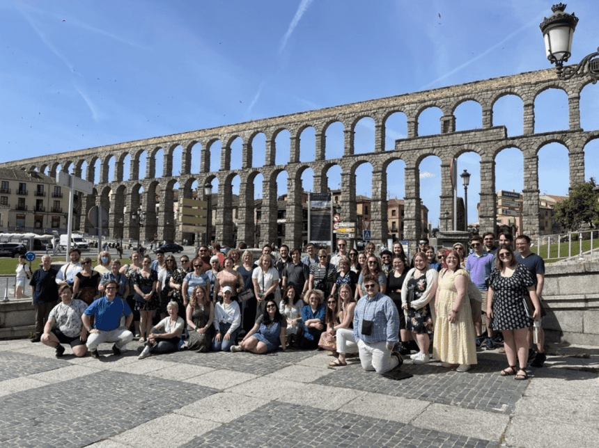 A group of people standing and sitting in front of an arch wall. 