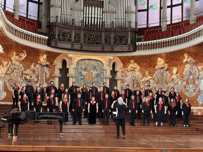 A choir group standing next to a piano being directed. 