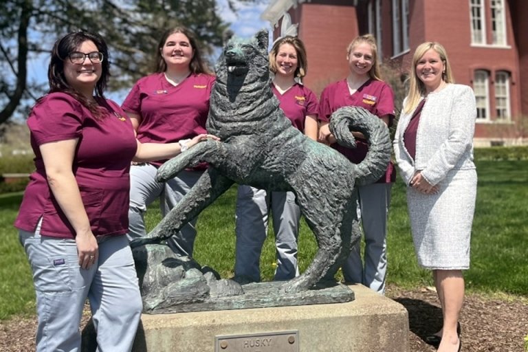 A group of people standing around a husky statue. 