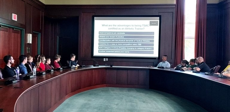 M.S Athletic Training Students around a table with a presentation on screen