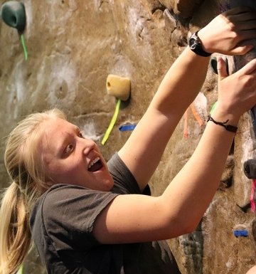 Student climbing rock wall indoors.