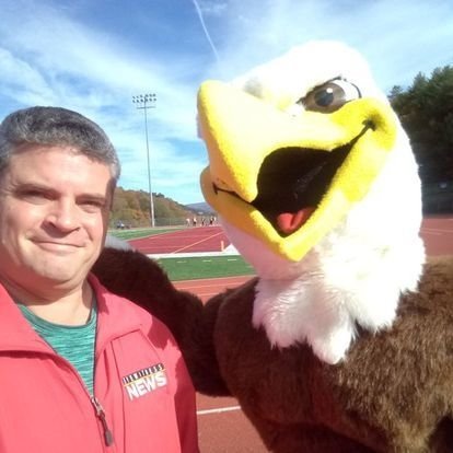 A man standing with an eagle mascot. 